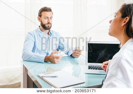 Male patient is holding a space chamber and an aerosol inhaler in front of a female doctor at her office