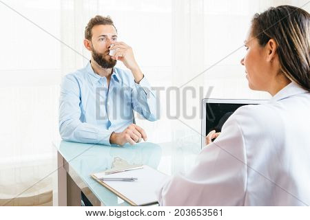 Male patient is inhaling a medicament from an aerosol inhaler in front o a female doctor at her office