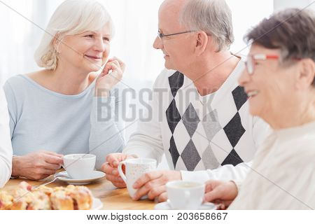 Close up of happy senior couple in love smiling looking at each other holding cups of coffee during meeting with elderly friends