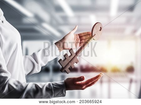 Business woman in white shirt keeping big stone key in hands with office view and sunlight on background. Mixed media.