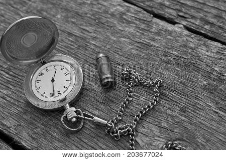 Retro watch with Roman Numerals laid next to the pistol cartridge. In black and white