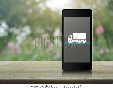 Truck flat icon on modern smart phone screen on wooden table over blur pink flower and tree Business transportation service concept