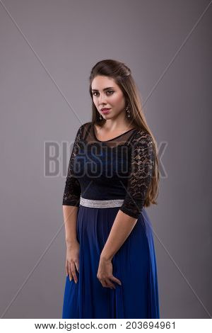 Portrait of a plus size female model posing in black dress over grey background. Beautiful woman with curvy figure.