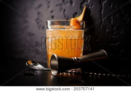 orange cocktail in crystal glass with bar spoon and jigger on black background