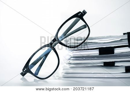 Close up black reading eyeglasses on stacking of office paper business working document and information data concept.