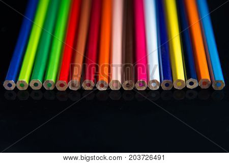Multicolored pencils on a black background are arranged in a line