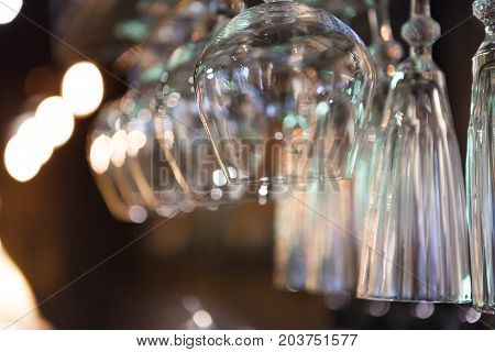Glasses hanging on bar rack close up. Clean utensil for wine and cognac in restaurant, barroom background