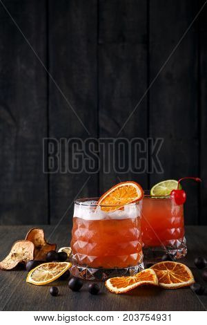 Cocktail on rustic wood background. Cold citrus alcohol beverage with tequila, blood orange juice and ginger beer, served with ice, citrons and chocolate snacks, copy space