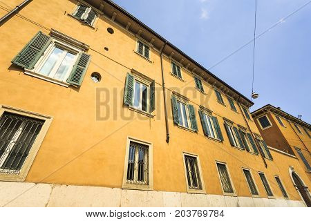 A house facade with many windows with green blinds in a sunny day with blue clean sky.