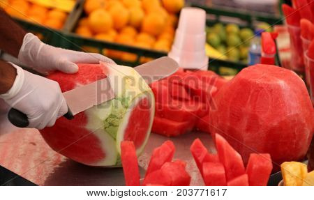 Skilled Grocer Cuts The Watermelon With A Large, Sharp Knife To