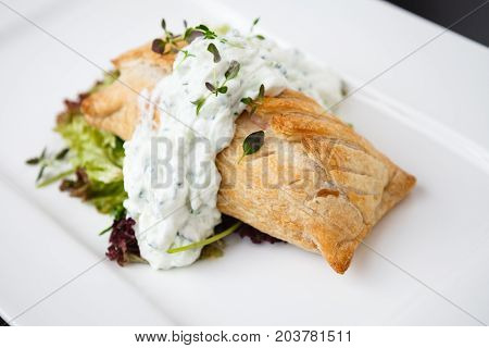 Traditional russian pie - coulibiac. Baked puff pastry filled with smoked salmon, served with sour cream sauce