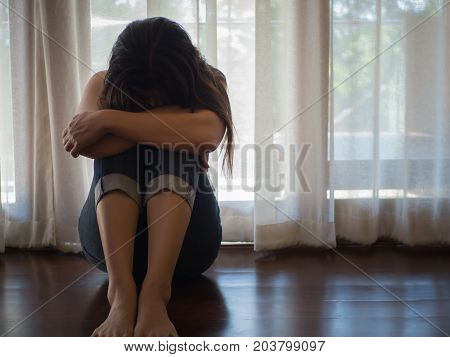 Sad and despaired woman hug her knee and cry while sitting alone on the floor.