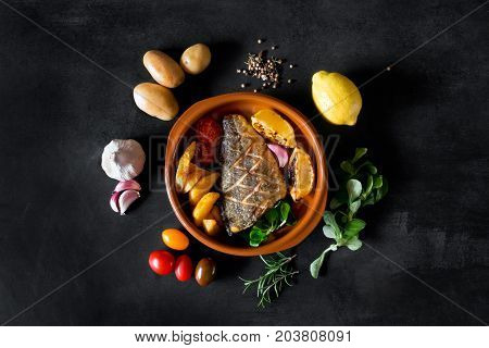 Baked dorado with fresh salad, vegetables and potato chips. Plate is surrounded by fresh ingredients