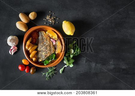 Baked dorado with fresh salad, vegetables and potato chips. Plate is surrounded by fresh ingredients