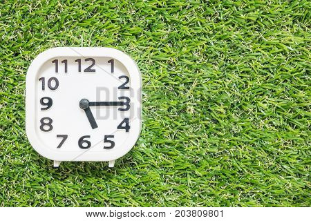 Closeup white clock for decorate show a quarter past five o'clock or 5:15 p.m. on green artificial grass floor textured background with copy space
