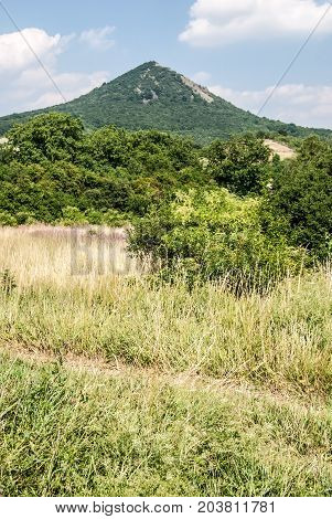 meadow with pathway small forest and isolated Lovos hill in Ceske stredohori mountains above Lovosice hill in Czech republic