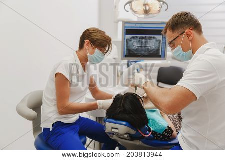 A Male Dentist With A Female Assistant Helps To Treat The Teeth Of A Woman Patient In A Clinic In Th