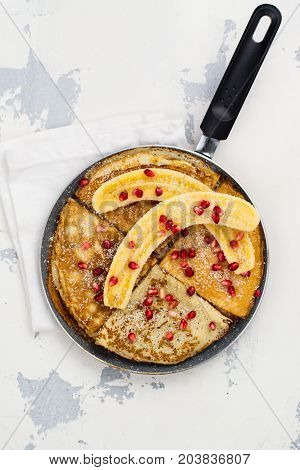 Sweet crepes with banana, honey and pomegranate seeds in a frying pan. Delicious family breakfast concept. Space for text