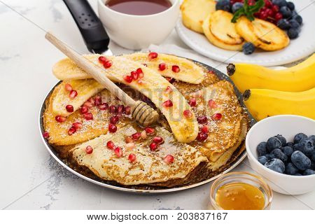 Sweet crepes with banana, honey and pomegranate seeds in a frying pan. Delicious family breakfast concept. Space for text
