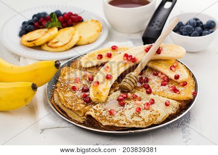 Sweet crepes with banana, honey and pomegranate seeds in a frying pan. Delicious family breakfast concept. Space for text