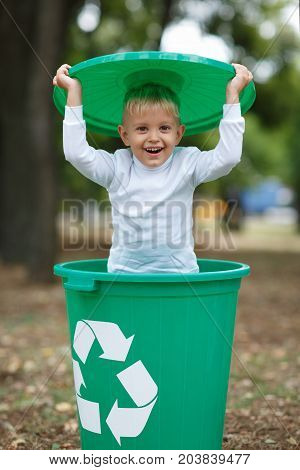 Cute preschooler, standing boy playing with the trash bin lid, in the street, summer outdoor, save the planet, save the Earth concept. Day in park. Funny babies.