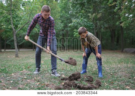 Two boys are planting plants. Two brothers a dig earth in a park for planting a young tree. Image of brothers farmers digging in the garden. Prepare for the planting.