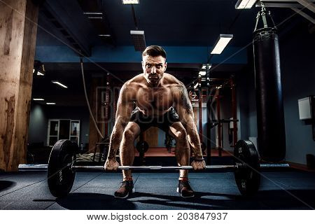 Muscular strong fitness man doing deadlift of a barbell in modern fitness center. Functional training. Snatch exercise. Scream for motivation