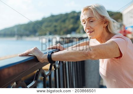 Regaining breath. Pleasant senior woman leaning on the balustrade of the bridge and regaining her breath while resting after a morning run