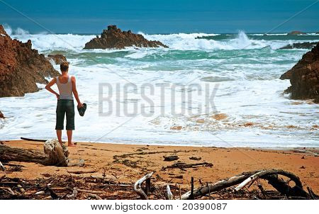 Vista oceano tempestoso con una donna in piedi sulla spiaggia di sabbia, serata a Knysna, Sudafrica