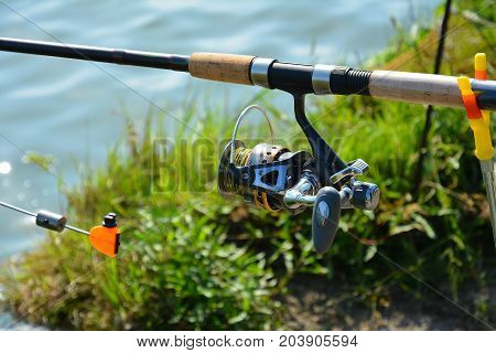 Tackles for fishing: rod with a coil. Fishing on the river bank in the summer morning.