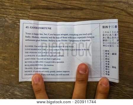 KYOTO, JAPAN - JULY 05, 2017: Close up of a hand with a fortune paper over a wooden background in Kyoto, Japan.