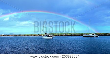 Natures beauty a colourful vibrant Rainbow in a stormy blue sky over water with boats next to a break-wall. Photographed in the safe haven of Iluka harbour on the Clarence river New South Wales Australia.