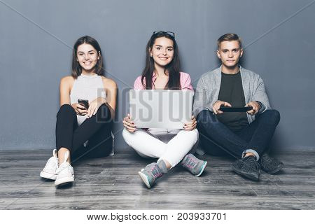 Three Young Friends Use Devices On The Floor In Living Room