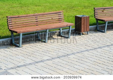 Two stylish benches and a trash can in a summer park along a paved path against a green lawn. Small architectural forms concept