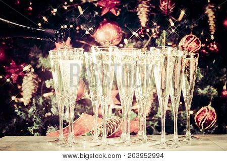 Filling Up Glasses For Party. Glasses Of Champagne With Christmas Tree Background And Sparkles. Holi