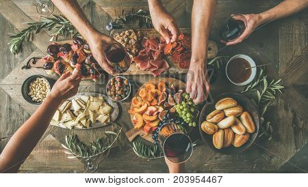 Flat-lay of friends hands eating and drinking together. Top view of people having party, gathering, celebrating together at wooden rustic table set with different wine snacks and fingerfoods