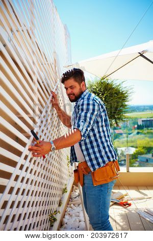 Young Adult Man Decorating The House Wall, By Setting Up The Wooden Trellis For Climbing Plants