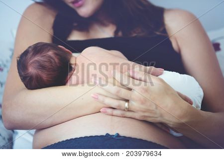 Young Mother Breastfeeds Her Baby, Holding Him In Her Arms And Smiling