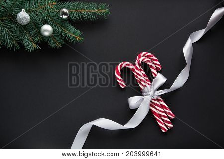 Christmas candy with silver ribbon and green fir tree on black background. Christmas background. Top view and copy space.