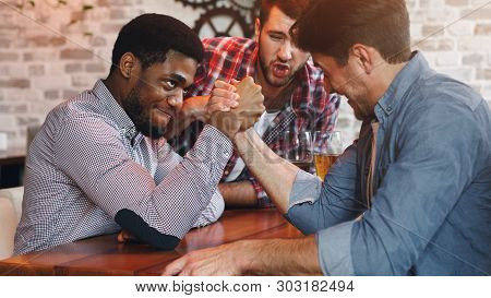 Diverse Friends Arm Wrestling And Drinking Beer At Bar Or Pub