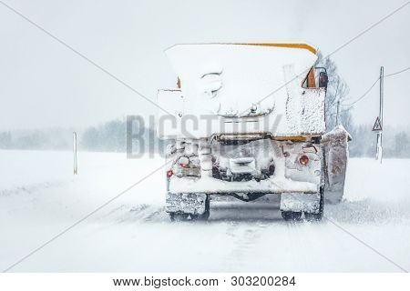 Plow Gritter Truck On Snow Covered Road During Snowstorm, View From Car Behind