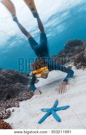 Woman snorkeling and skin diving in the tropical sea and gets closer to the blue starfish lying on the sandy bottom. Focus on the modelâs face