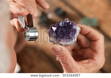 Male Jeweler Evaluating Semi Precious Gemstone At Table In Workshop, Closeup
