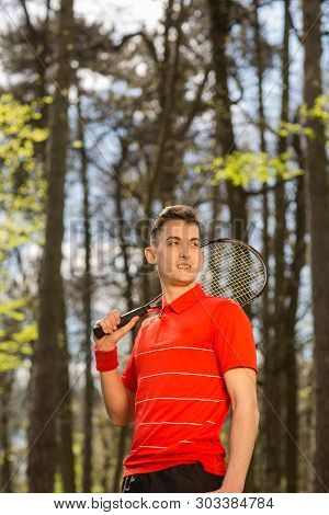 The Man In A Red T-shirt Pose With A Tennis Racket And Orange Thermocouple, On The Background Of Gre
