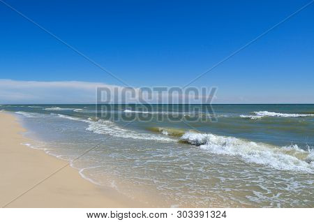 Sea Waves Wash The Beach Against A Blue Sky. Landscape On A Wild Beach. The Sea In The Summer.