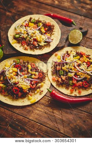 Healthy corn tortillas with grilled beef, fresh hot peppers, cheese, tomatoes over rusty wooden table background, top view, copy space. Mexican food contept.