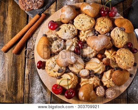 Oatmeal cookies and sand chocolate cake with cherry berry on cutting board on wooden table in rustic style. Top view of cinnamon stick still life.