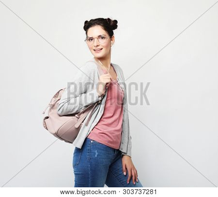 young brunette woman wearing a pink t-shirt and jeans is holding a backpack and smiling