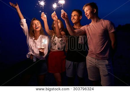 Friends Walking, Dancing And Having Fun During Night Party At The Seaside With Bengal Sparkler Light