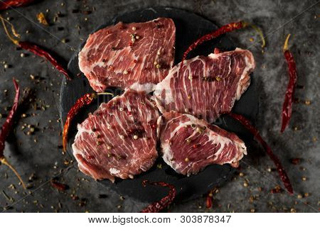 high angle view of some pieces of raw secreto iberico, a pork cut from spanish iberian pig, on a black slate tray, placed on a gray stone table or countertop